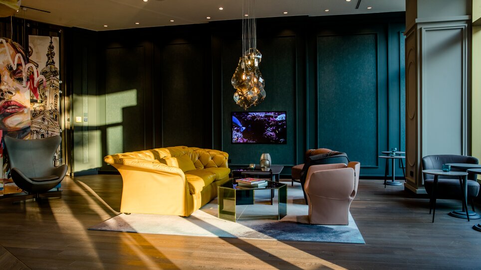 Stylische Lounge mit gelbem Sofa, Kunst und TV. | © Motel One Austria GmbH