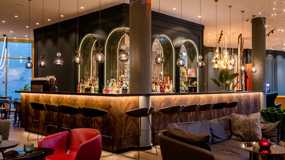 Elegante Bar mit stilvollem Design und beleuchteten Regalen. | © Motel One Austria GmbH