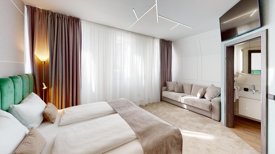 Camera doppia moderna con tende chiare e divano accogliente. | © NED Hotel