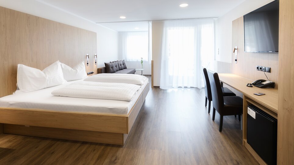 Luminoso camera doppia con arredi in legno e divano. | © Ulrike Rauch