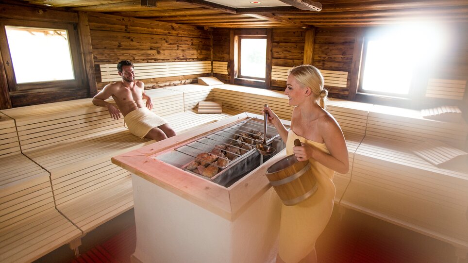 Sauna con due persone, una con un secchio, una sulla panca. | © Novapark 