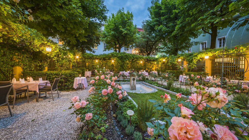 Romantic garden with roses, laid tables and stylish evening lighting. | © Parkhotel Graz
