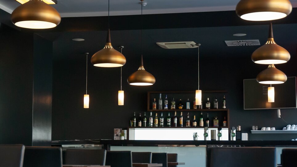 Interior of a restaurant featuring hanging lamps and a bar in the background. | © PLAZA INN Graz City