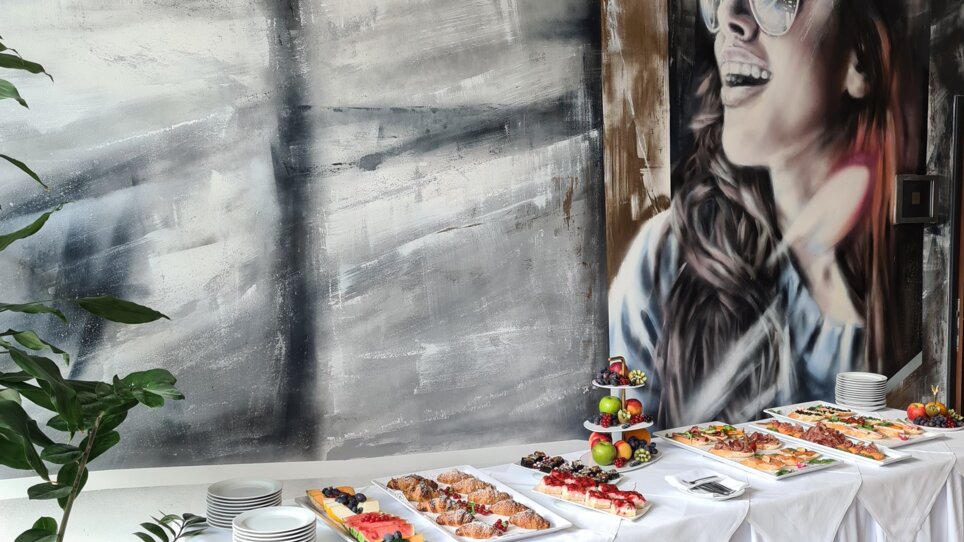 A buffet with various dishes in front of a mural of a smiling woman. | © PLAZA INN Graz City