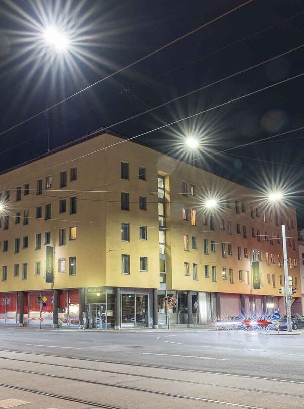 Illuminated city area in Graz at night, featuring PLAZA INN Graz City and street lamps. | © PLAZA INN Graz City - Martin Thalmann