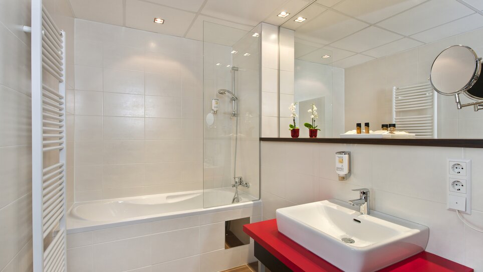 Bright bathroom with bathtub, sink, and mirror. | © PLAZA INN Graz City - Harald Eisenberger