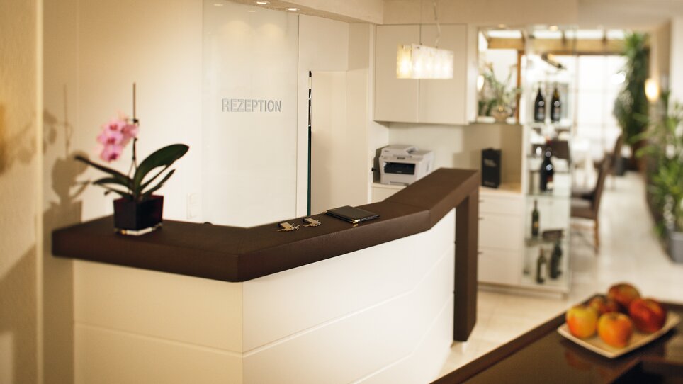 Modern hotel lobby with reception desk and plants. | © Roemerstube