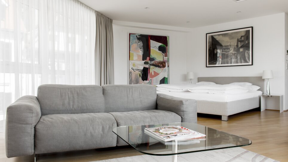 Modern double room with sofa, table, and floor-to-ceiling windows. | © Schlossberghotel