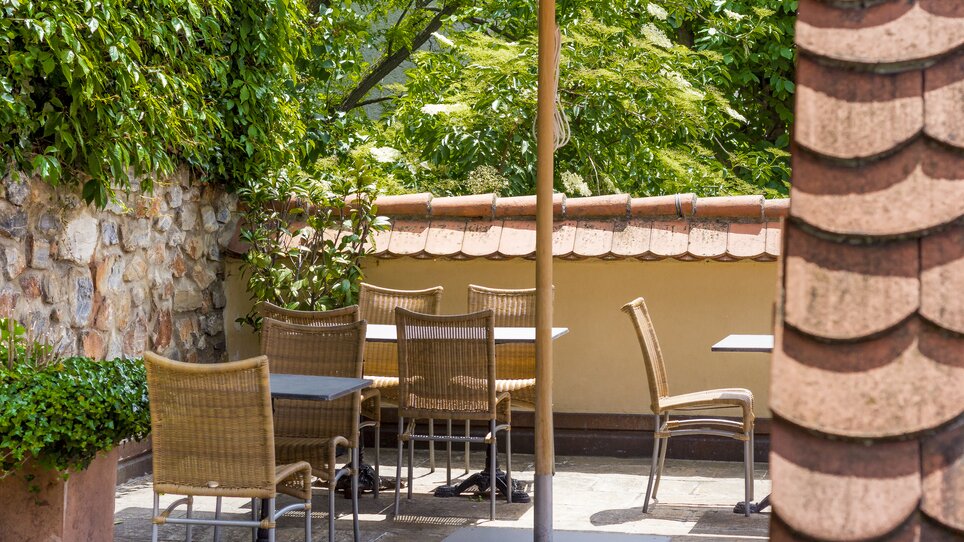 Cozy terrace with tables and chairs surrounded by plants. | © Schlossberghotel