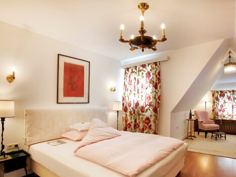 Bright double room with red wall art and floral curtains. | © Schlossberghotel