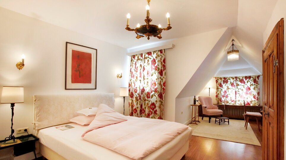 Bright double room with red wall art and floral curtains. | © Schlossberghotel