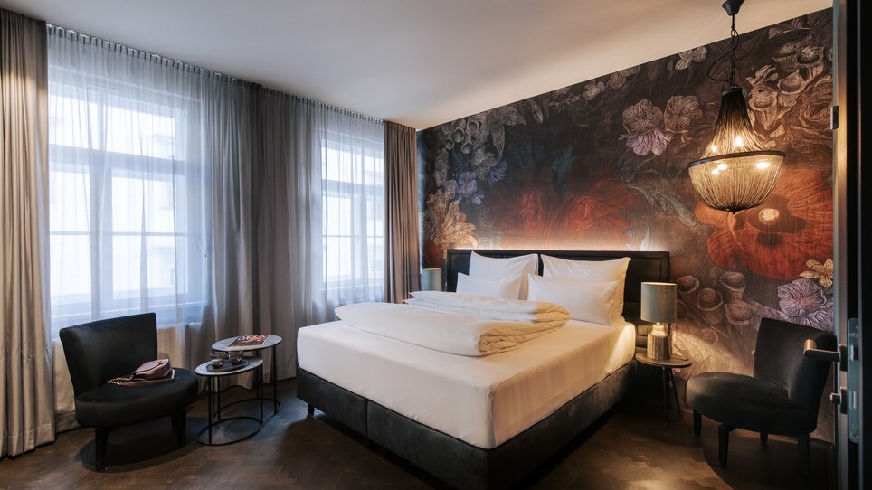 Elegantes Zimmer mit einem großen Bett und stilvollem Wanddesign im Aiola Living. | © Aiola Living