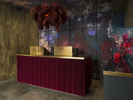 Modern hotel reception with red velvet, gold accents, and floral patterns. | © Aiola Living