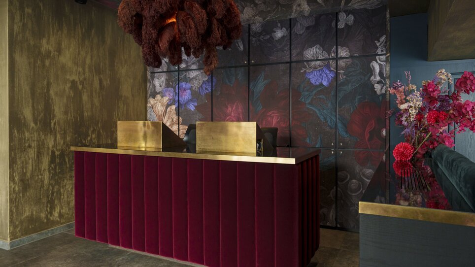Moderne Hotelrezeption mit rotem Samt, goldenen Akzenten und Blumenmuster. | © Aiola Living