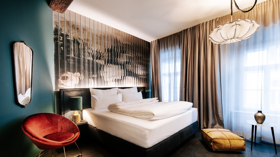 Stilvolles Zimmer mit Bett, stimmungsvollem Licht und Kunstwerk. | © Aiola Living