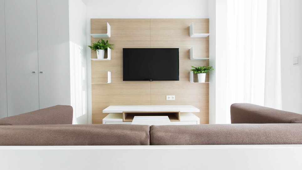 Soggiorno luminoso con divano, TV e piante. | © sHome Hotel