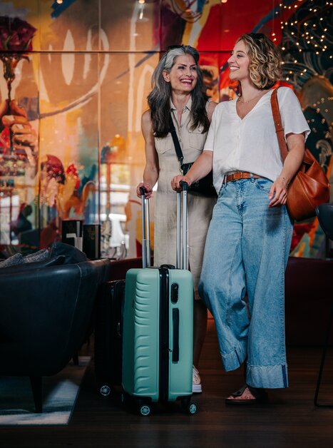 Zwei Frauen lächeln mit Koffern in einem modernen Raum. | © Graz Tourismus - Mias Photoart