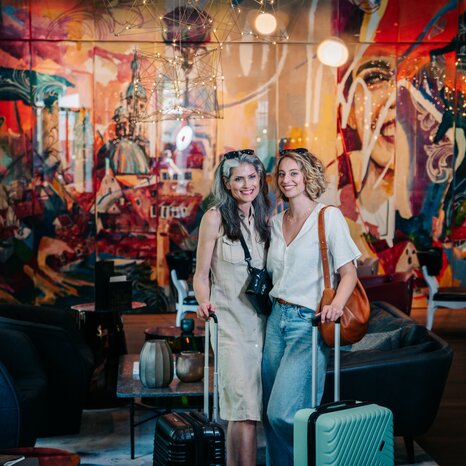 Two women with suitcases stand in a modern lobby. | © Graz Tourismus - Mias Photoart
